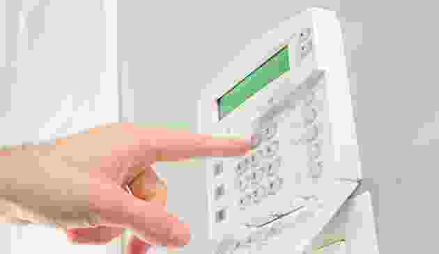 A hand pressing a button on a white security alarm keypad. A hand pressing a button on a white security alarm keypad.