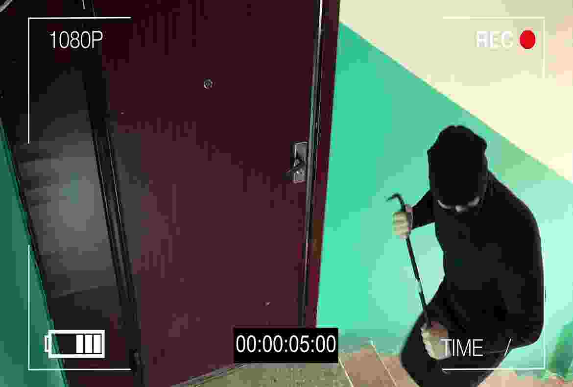 A person holds a gun behind a partially open door in a dimly lit room.
