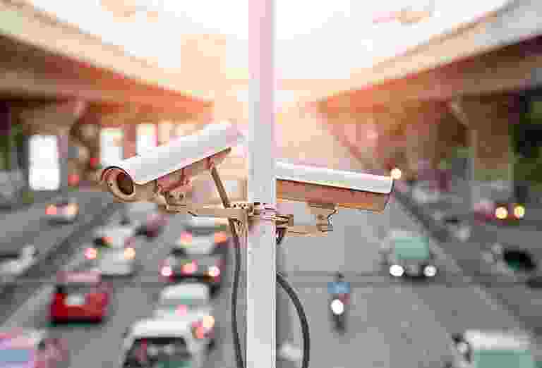 Two security cameras overlooking a busy street during sunset. Two security cameras overlooking a busy street during sunset.