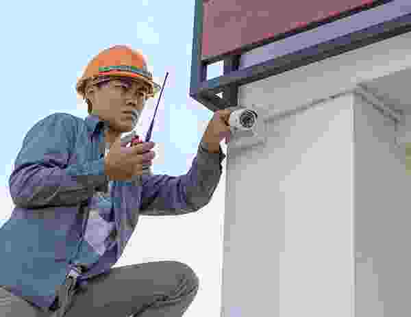 Technician installing a security camera on a building exterior. Technician installing a security camera on a building exterior.