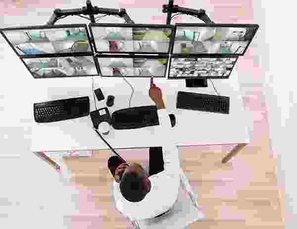 Person monitoring multiple surveillance screens at a workstation. Person monitoring multiple surveillance screens at a workstation.