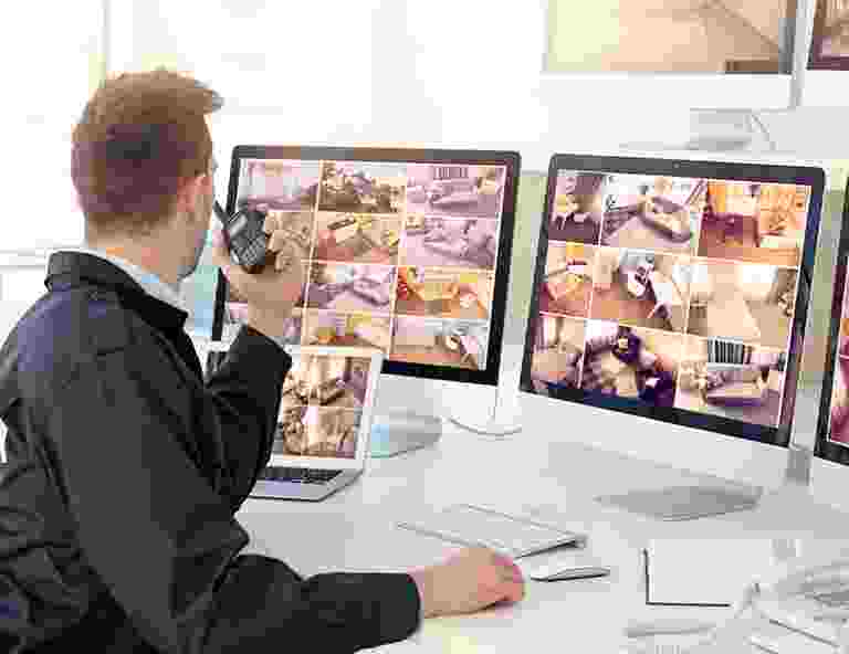 Man monitoring multiple security camera feeds on two screens. Man monitoring multiple security camera feeds on two screens.