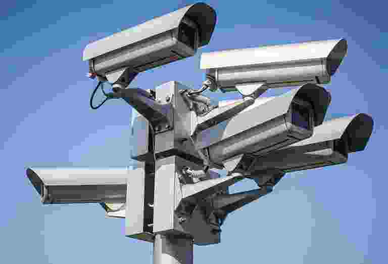 A cluster of security cameras mounted on a pole under a clear blue sky. A cluster of security cameras mounted on a pole under a clear blue sky.