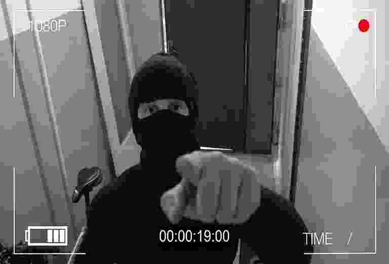 Person in black mask pointing at the camera indoors. Person in black mask pointing at the camera indoors.