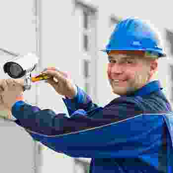 Technician installing a security camera while smiling. Technician installing a security camera while smiling.