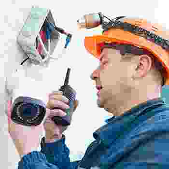 Technician installing a security camera and communicating via walkie-talkie. Technician installing a security camera and communicating via walkie-talkie.