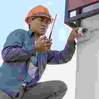Technician inspecting security camera installation outdoors. Technician inspecting security camera installation outdoors.