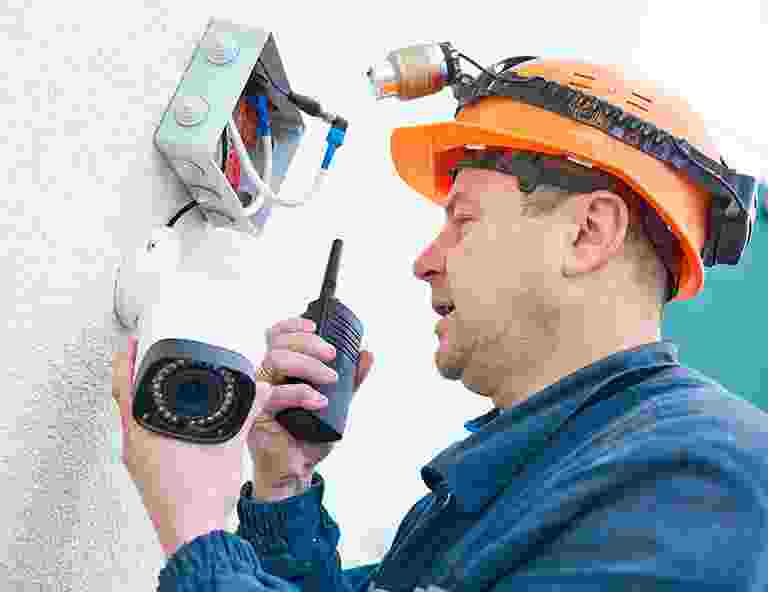 Technician installing a security camera using a walkie-talkie. Technician installing a security camera using a walkie-talkie.