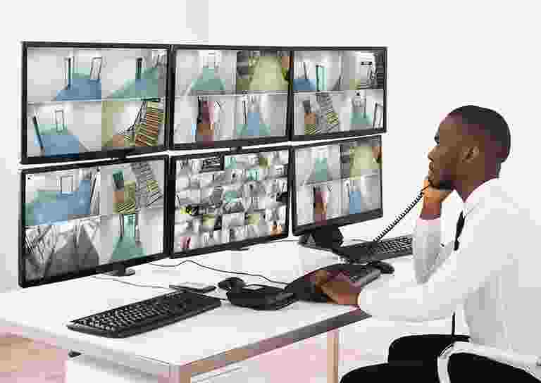 Man monitors multiple security camera feeds on large screens in a control room. Man monitors multiple security camera feeds on large screens in a control room.